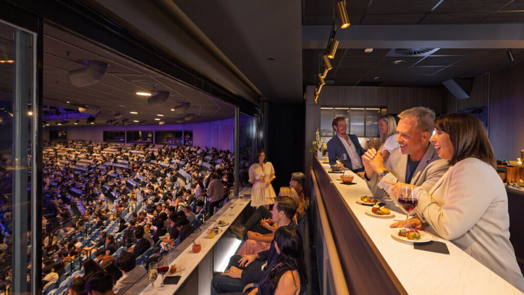 A group of people enjoying food and drink at a corporate event in a Rod Laver Arena suite.