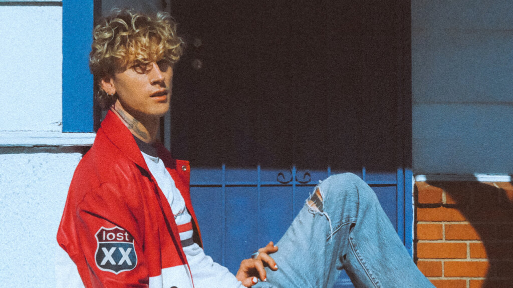 Singer mgk sitting and posing for the camera against a house backdrop.