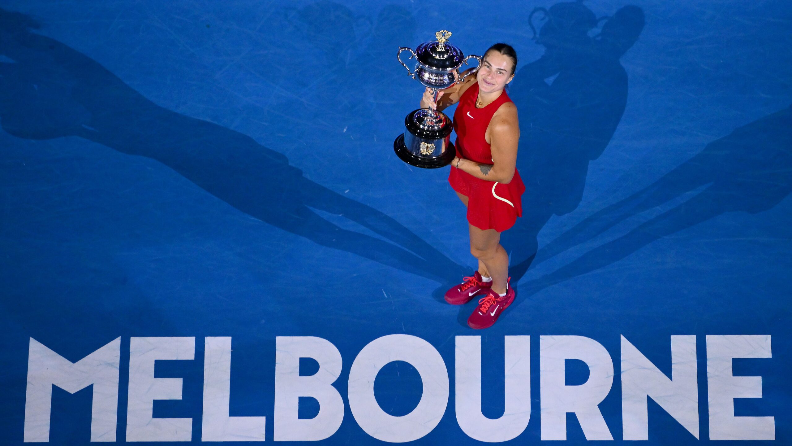 A woman proudly holds a tennis trophy on a blue court, celebrating her victory at the Australian Open.